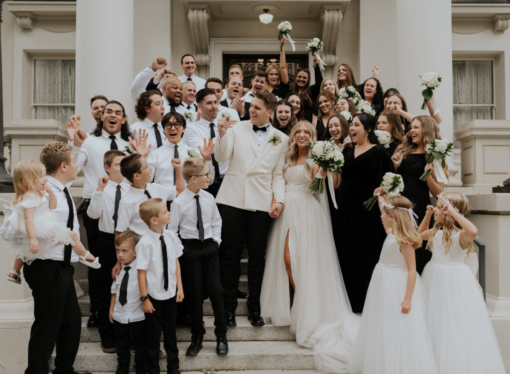 A bridal party cheering with the bride and groom to celebrate their wedding day captured by a photo video team