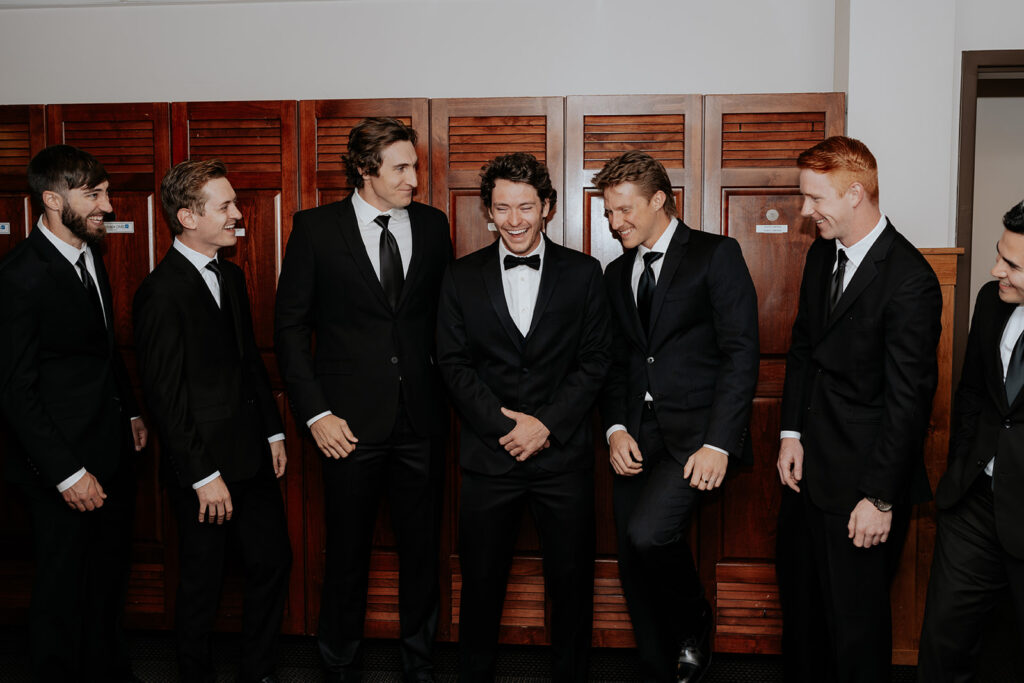 a groom hanging out with his groomsmen in the locker room on his wedding day 