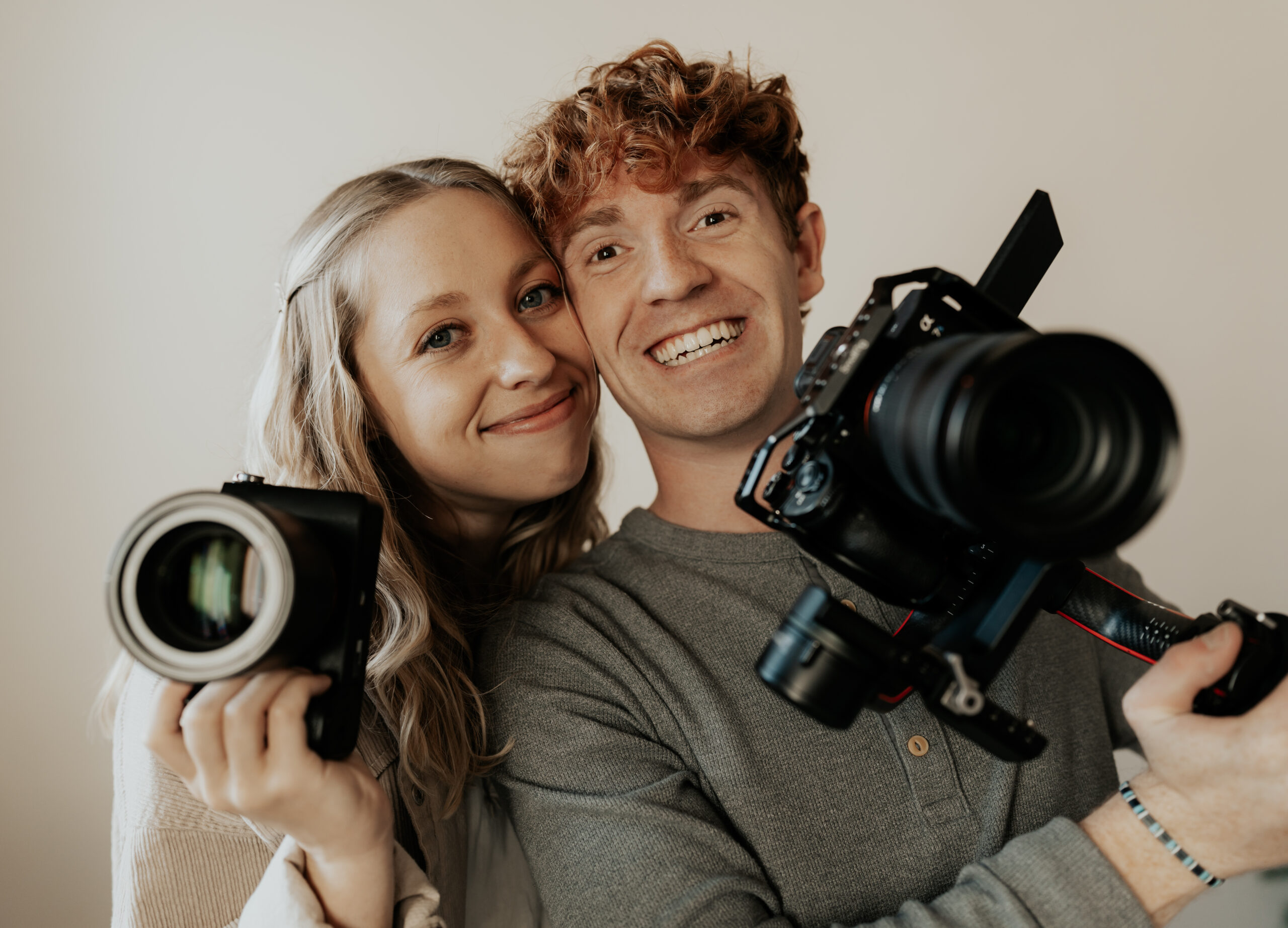 a husband and wife photographer/videographer team smiling with their cameras