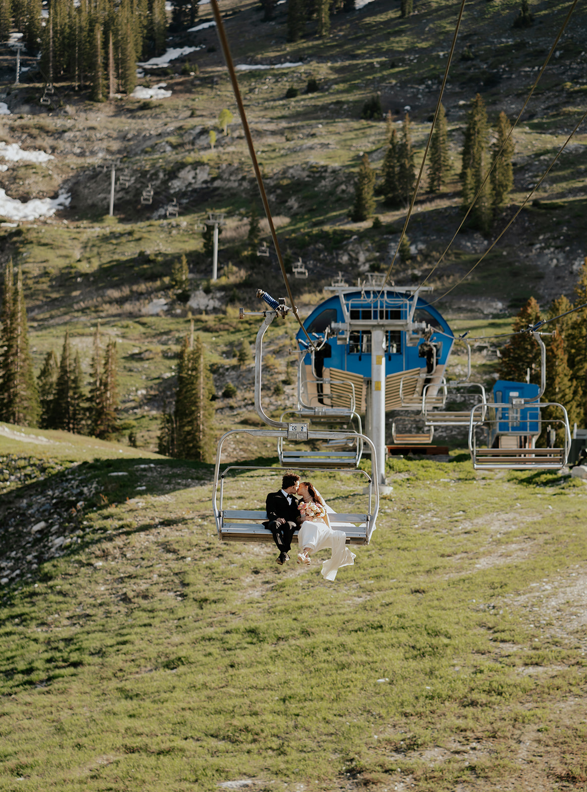 a bride and groom kissing on a ski lift after their mountain resort wedding