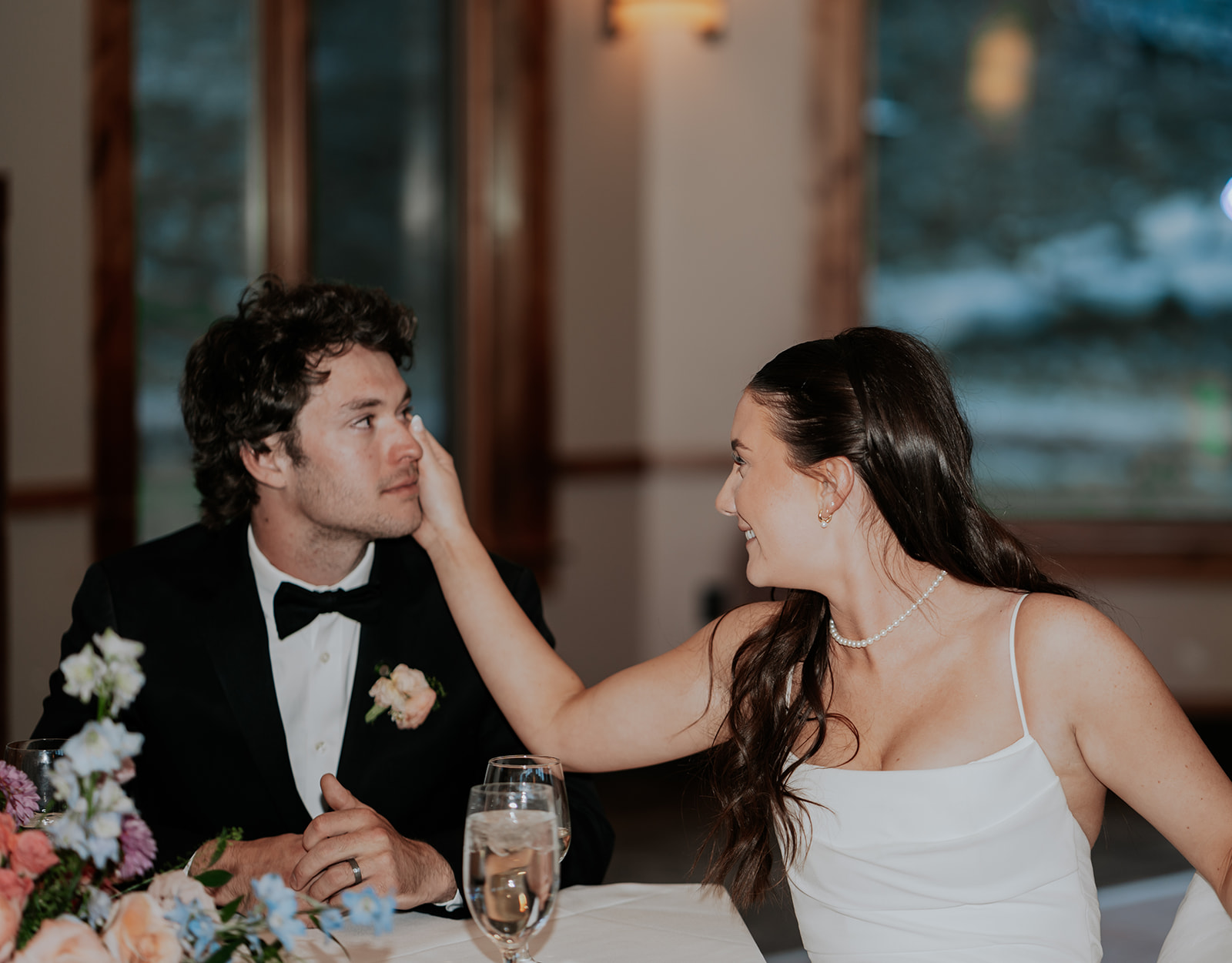 a bride wiping a tear from the grooms face while they listen to speeches at their wedding at Solitude Ski Resort